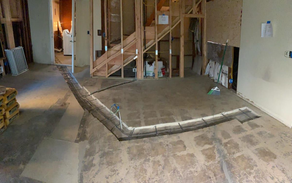 A room taken down to the studs and the bare slab, with a patched trench curving across the concrete floor